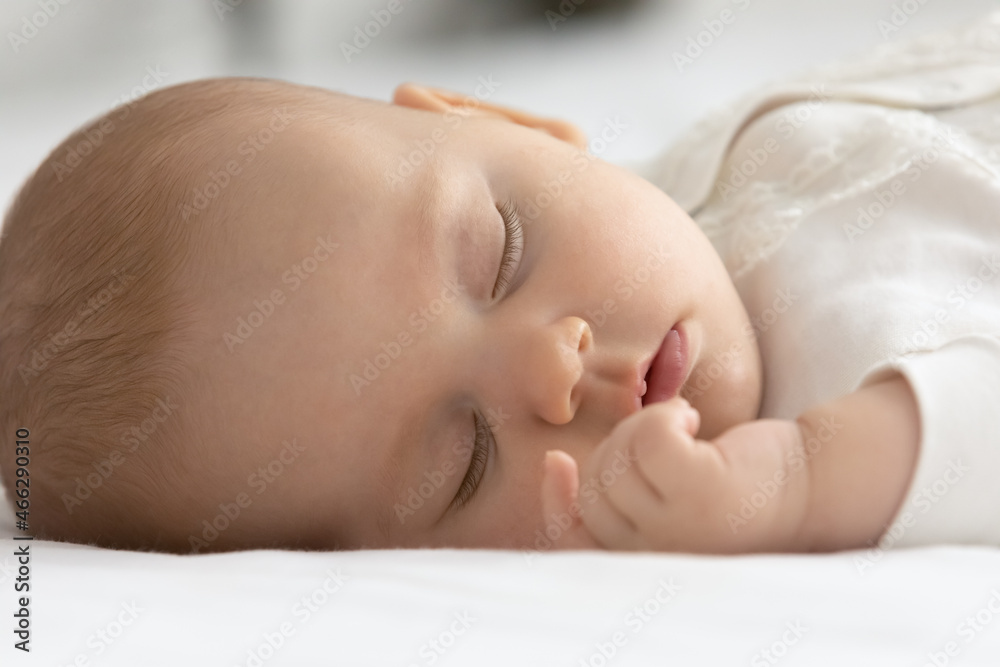 Close up cute newborn baby with closed eyes lying on white cozy bed, taking day nap, small Caucasian child kid sleeping, relaxing, dreaming resting alone, fall asleep, childhood concept Close up cute newborn baby with closed eyes lying on white cozy bed, taking day nap, small Caucasian child kid sleeping, relaxing, dreaming resting alone, fall asleep, childhood concept