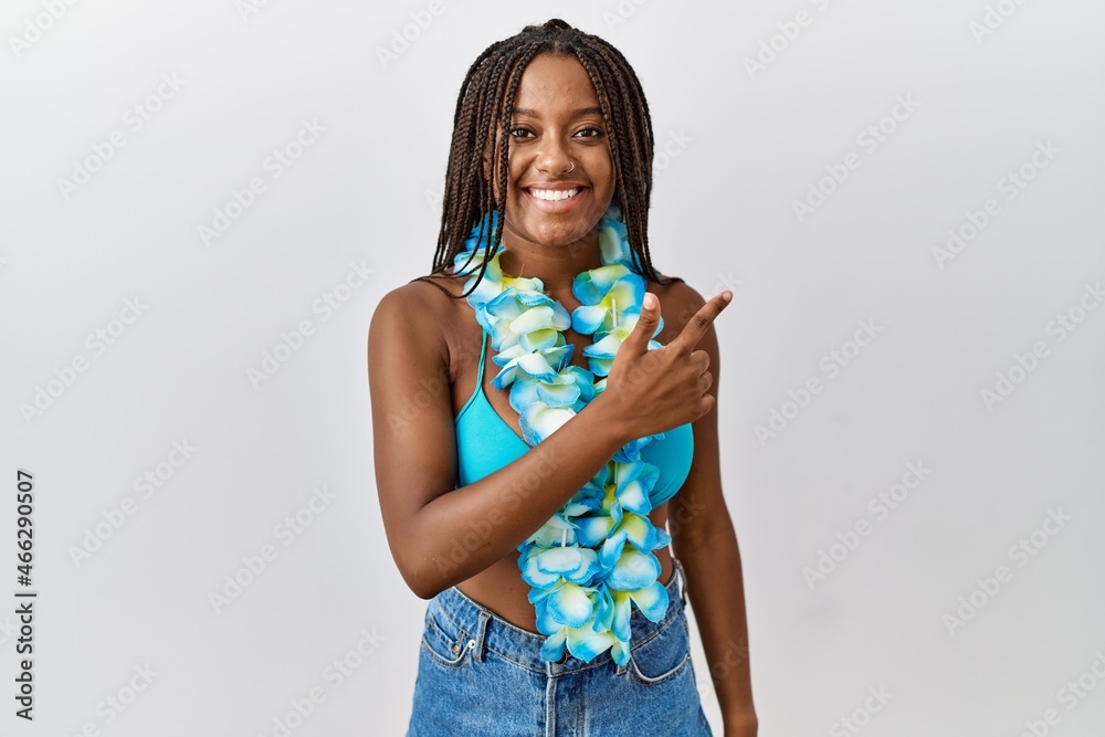 Young african american woman with braids wearing bikini and hawaiian lei cheerful with a smile of face pointing with hand and finger up to the side with happy and natural expression on face Young african american woman with braids wearing bikini and hawaiian lei cheerful with a smile of face pointing with hand and finger up to the side with happy and natural expression on face