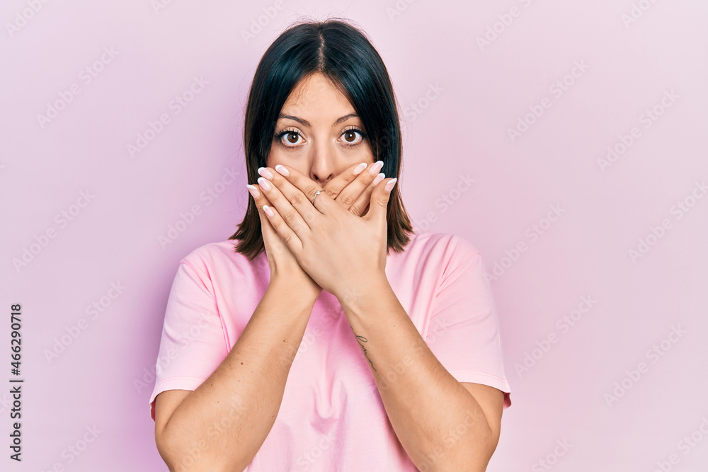 Young hispanic woman wearing casual pink t shirt shocked covering mouth with hands for mistake. secret concept. Young hispanic woman wearing casual pink t shirt shocked covering mouth with hands for mistake. secret concept.