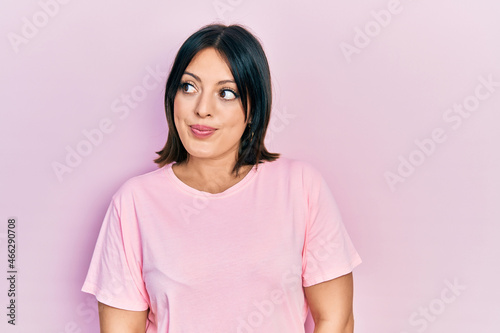 Young hispanic woman wearing casual pink t shirt smiling looking to the side and staring away thinking.