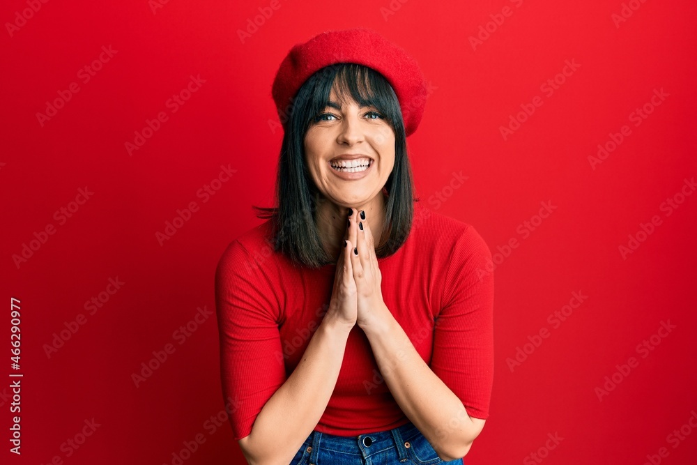 Young hispanic woman wearing french look with beret praying with hands together asking for forgiveness smiling confident. Young hispanic woman wearing french look with beret praying with hands together asking for forgiveness smiling confident.