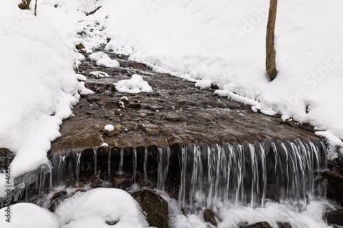 Small waterfall of cold water flow among the stones covered with snow © YouraPechkin