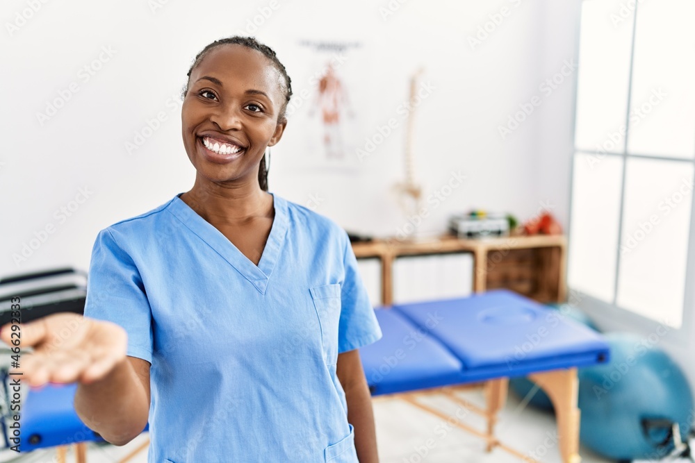 Black woman with braids working at pain recovery clinic smiling cheerful offering palm hand giving assistance and acceptance. Black woman with braids working at pain recovery clinic smiling cheerful offering palm hand giving assistance and acceptance.