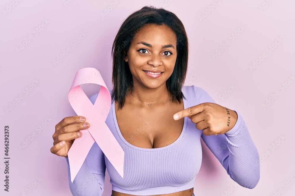 Young african american girl holding pink cancer ribbon pointing finger to one self smiling happy and proud Young african american girl holding pink cancer ribbon pointing finger to one self smiling happy and proud