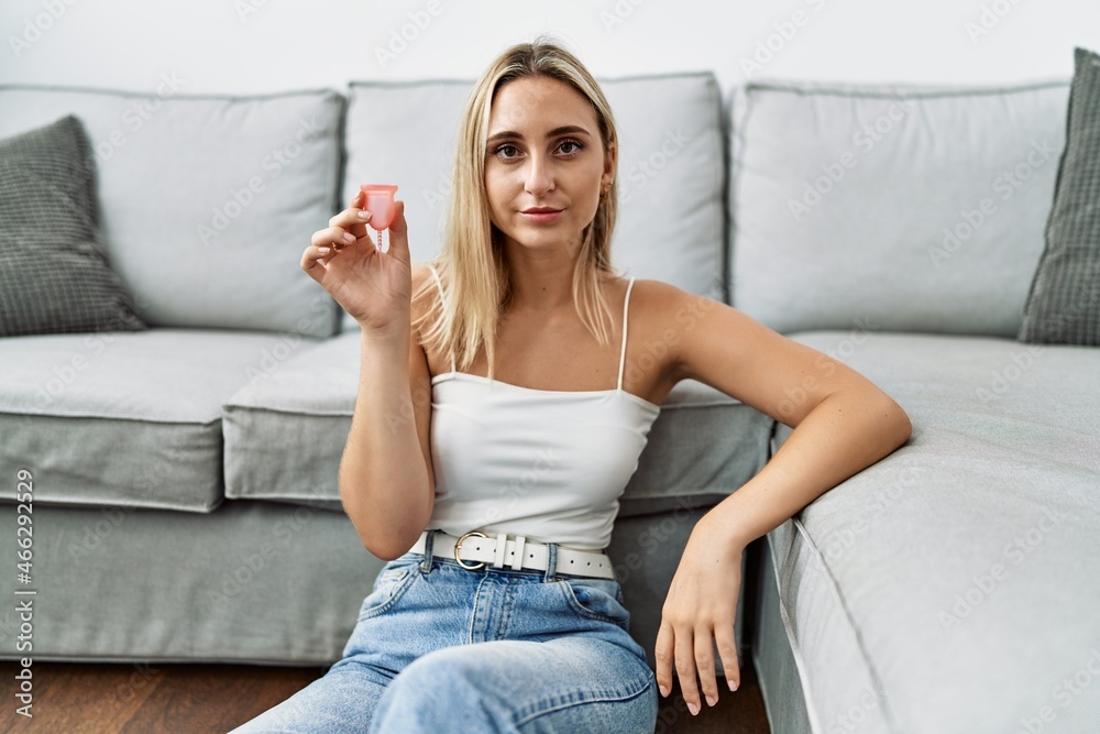 Obraz premium Young blonde woman holding menstrual cup thinking attitude and sober expression looking self confident