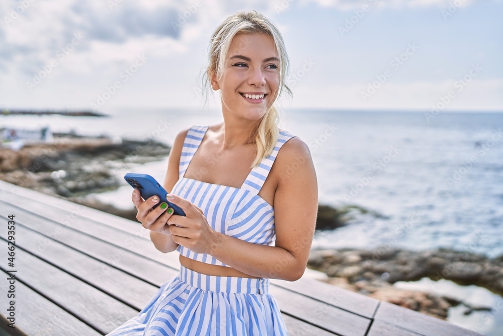 Young blonde girl using smartphone sitting on the bench at the beach.