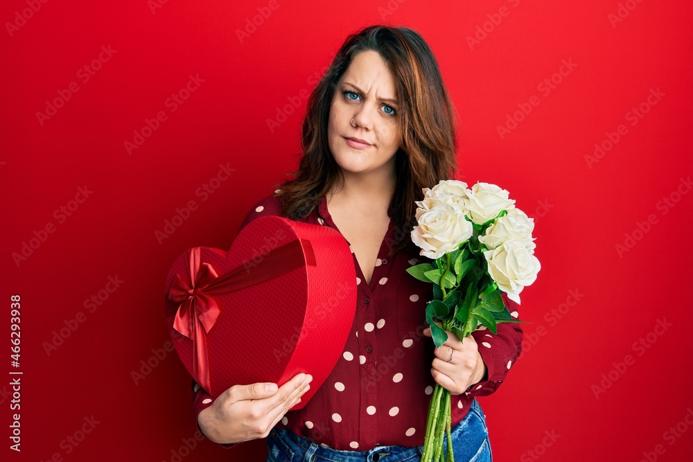 Young caucasian woman holding valentine gift and flowers clueless and confused expression. doubt concept.