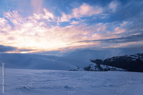 Fluffy clouds shelter under white snow sheltered by forests and beautiful mountains