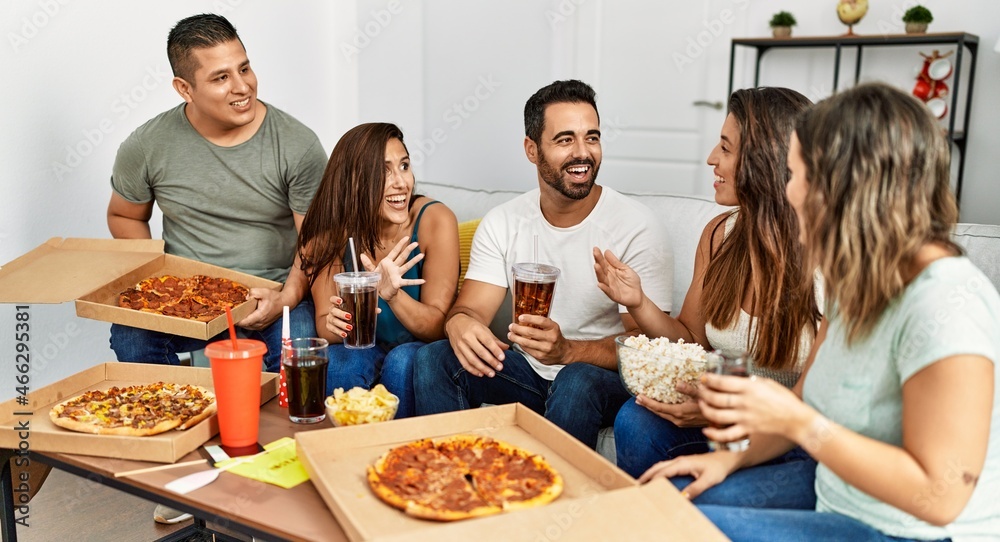 Group of young hispanic friends smiling happy eating italian pizza sitting on the sofa at home.
