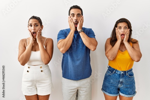Group of young hispanic people standing over isolated background afraid and shocked, surprise and amazed expression with hands on face