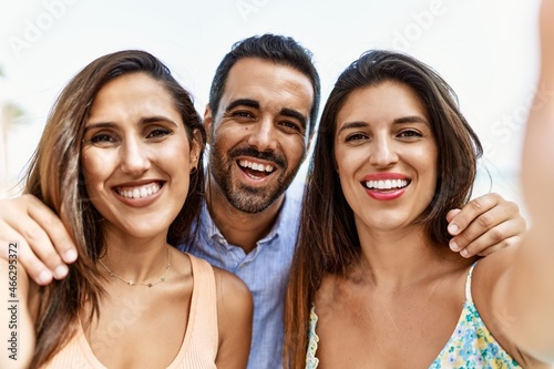 Three young hispanic friends smiling happy and hugging make selfie by the camera at the beach.