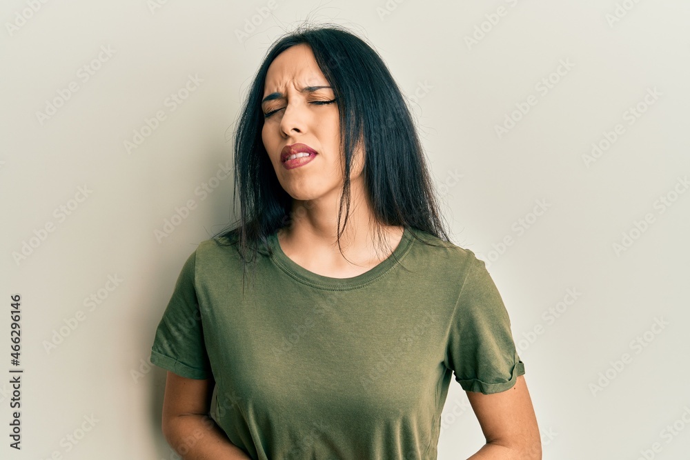 Young hispanic girl wearing casual t shirt with hand on stomach because nausea, painful disease feeling unwell. ache concept. Young hispanic girl wearing casual t shirt with hand on stomach because nausea, painful disease feeling unwell. ache concept.