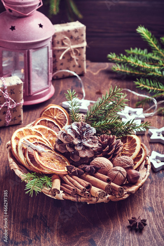 Valokuva Dry orange, star anise, cinnamon, pine cones and fir tree in rustic plate on wooden table