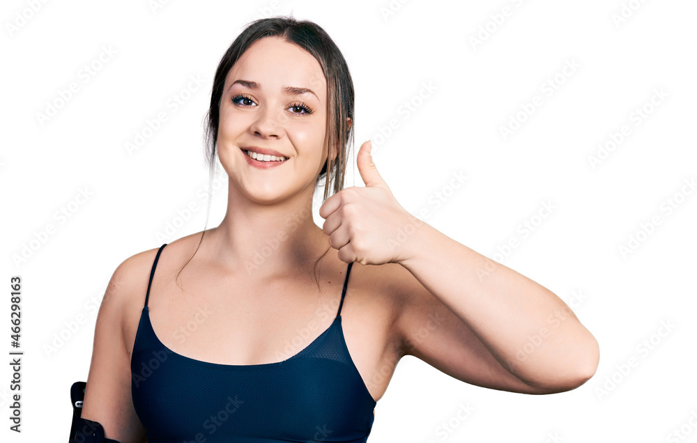Young hispanic woman wearing sportswear doing happy thumbs up gesture with hand. approving expression looking at the camera showing success. Young hispanic woman wearing sportswear doing happy thumbs up gesture with hand. approving expression looking at the camera showing success.