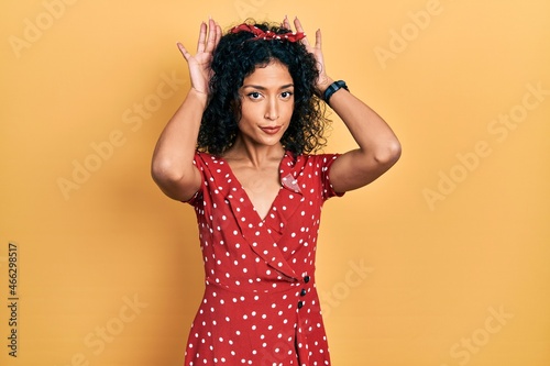 Young latin girl wearing summer dress doing bunny ears gesture with hands palms looking cynical and skeptical. easter rabbit concept.