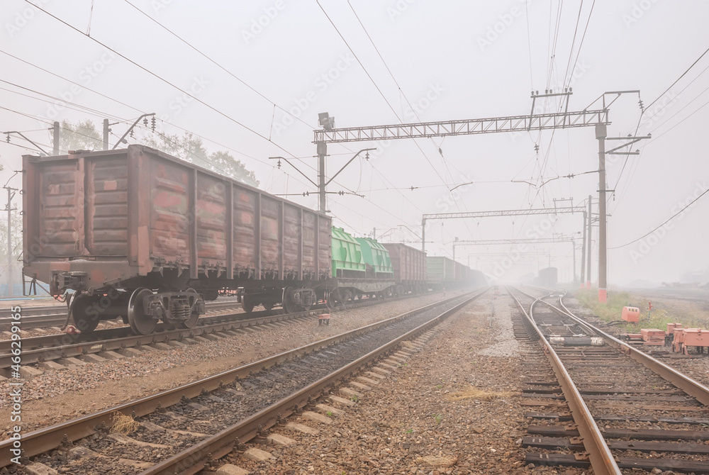 Freight terminal of railway trains. Railway tracks, cars and locomotive in fog.