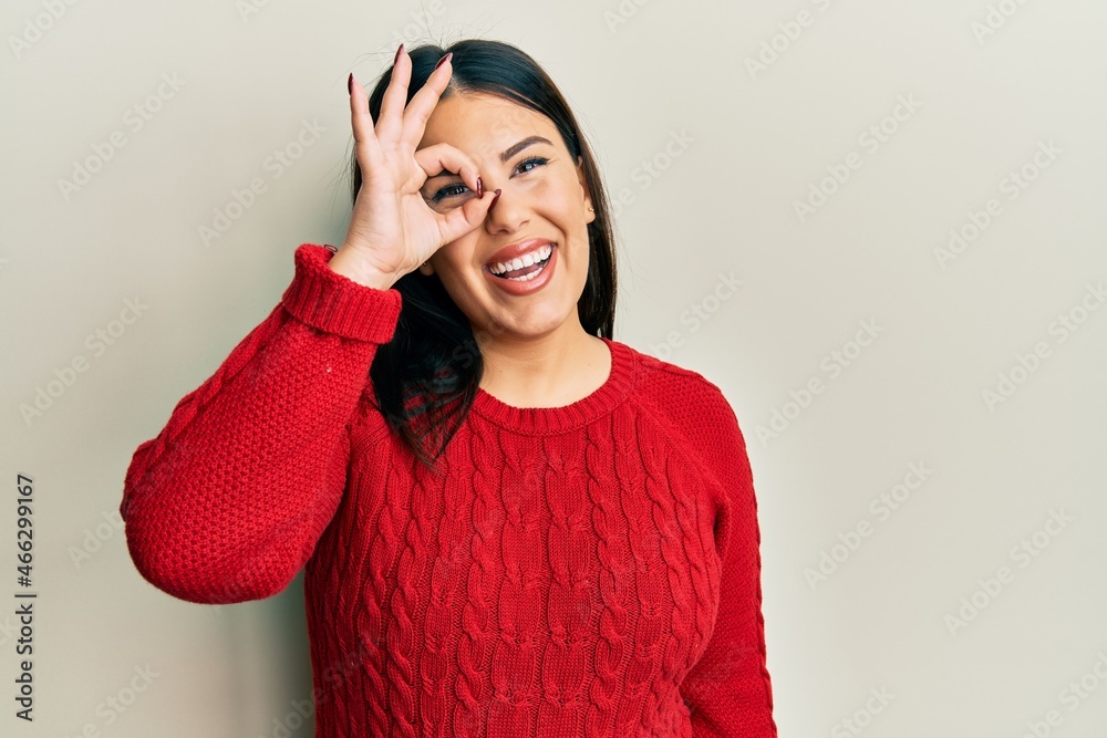 Beautiful brunette woman wearing wool winter sweater doing ok gesture with hand smiling, eye looking through fingers with happy face. Beautiful brunette woman wearing wool winter sweater doing ok gesture with hand smiling, eye looking through fingers with happy face.