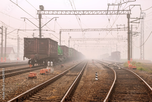 Freight terminal of railway trains. Railway tracks, cars and locomotive in fog.