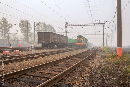 Freight terminal of railway trains. Railway tracks, cars and locomotive in fog.