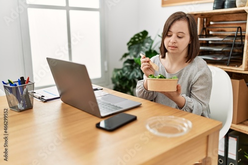 Brunette woman with down syndrome working eating salad at business office