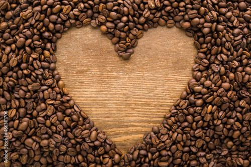 Heart shape created from fresh dark brown coffee beans. Empty place for text on wooden table background. Closeup. Top down view.