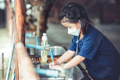 Cute little girl 4-5 years old wearing protective medical face mask washing her hands on sink in farm school. Sanitation and air pollution PM2.5 concept.