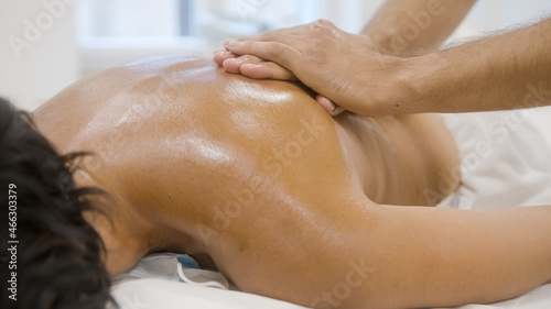 Masseurs hands giving a back massage to female patient using oil.