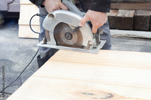 light wooden boards are sawn with an electric saw