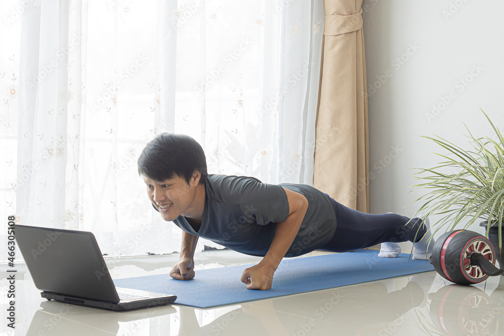Fototapeta premium Asian men enjoy exercising at home by watching online lessons through laptops. Free space.
