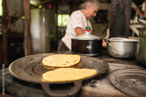 Primer plano de tortillas de maíz en un comal de una cocina de metal a la leña con una anciana de fondo photo