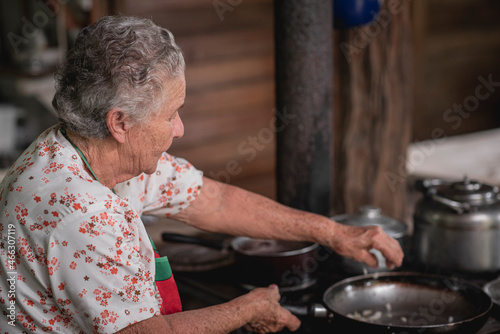 Retrato de una mujer adulta mayor cocinando en una estufa metálica con leña en su casa de madera  photo