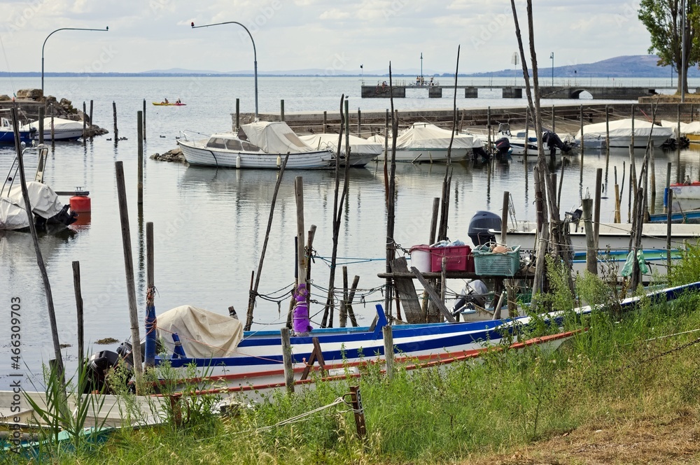 Fototapeta premium Small motor boats moored on wooden poles of the pier of a small port in Lake Trasimeno (Umbria, Italy, Europe)
