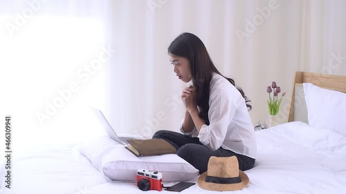 Young Asian woman sitting on the bed and preparing for trip, using a laptop computer to searching information for travel is opening a country after quarantine in hotel during the coronavirus outbreak. photo