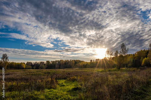 The sun s rays from under a large dark cloud fall on an autumn field with dry grass.
