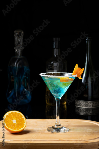 curaçao blue cacktail , blue margarita one on a wooden board blurred drink bottles on a dark background