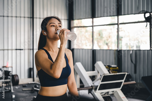 Asian young woman drinking water after workout in gym, healty and sport concept. © Natee Meepian
