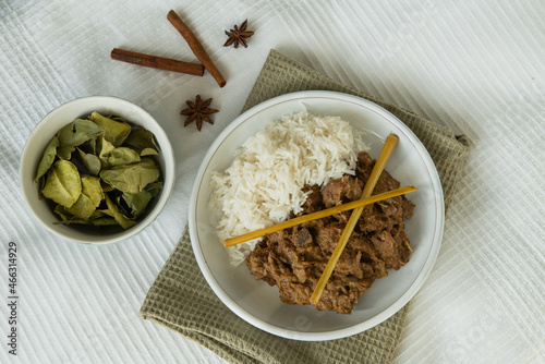 Vegan version of typical indonesian spiced meal, rendang cooked with jackfruit instead of the meat, served with rice and lemon grass, small bowl with dried kaffir leaves, cinnamon rolls and star anise