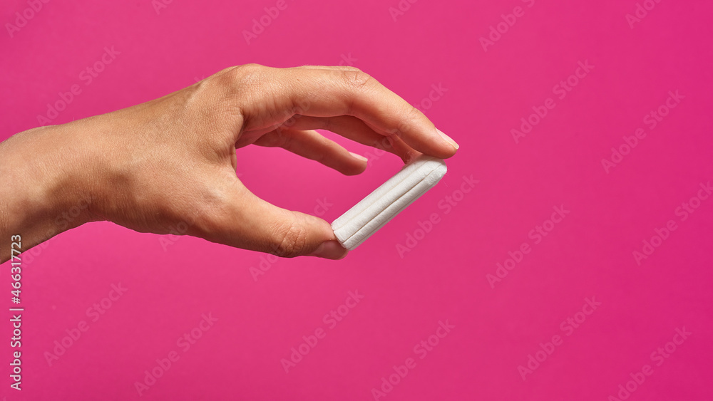 hygienic tampon in a female hand on a pink background