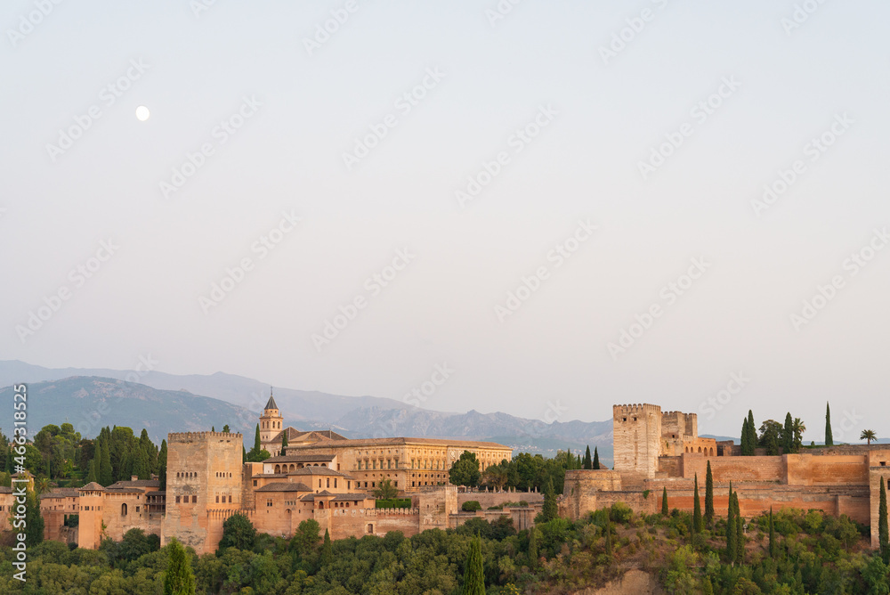 Landscape view of the famous Alhambra at sunset, Granada, Andalusia, Spain. White moon on the left. Pale blue sky on the background. With copy-space.