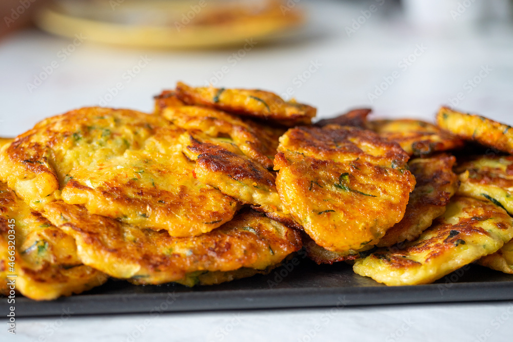 Close-up of pancakes made of zucchini and vegetables are laid out on a dark plate. A delicious vegetarian dish. Side view