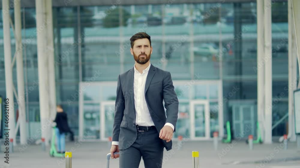 Caucasian bearded tourist businessman walks public transport building with luggage on urban background a city street. Man in formal suit trip. Business traveler pulling suitcase in airport terminal Caucasian bearded tourist businessman walks public transport building with luggage on urban background a city street. Man in formal suit trip. Business traveler pulling suitcase in airport terminal