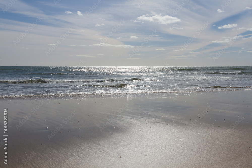 Front view of sea waves reaching the wet sand and sky with clouds 