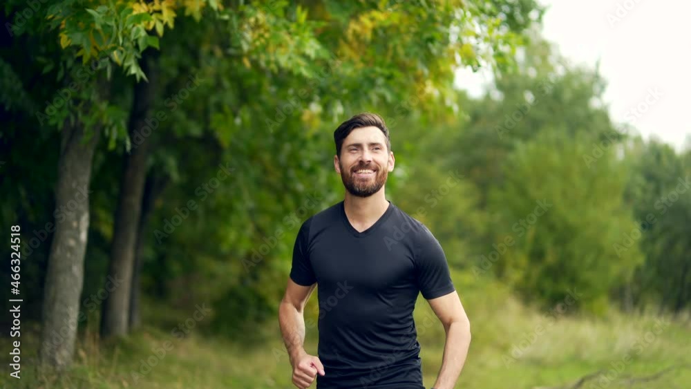Young Caucasian bearded happy man runner jogging in the forest or city park. Morning jog. Active healthy lifestyle fitness. Sport workout outdoor. Athlete training run exercise in the fresh air