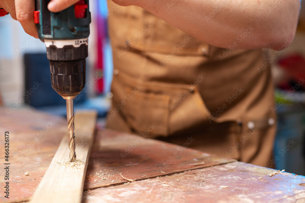 Carpenter drills a hole in wooden plank with an electrical drill. Joiner working in carpentry workshop