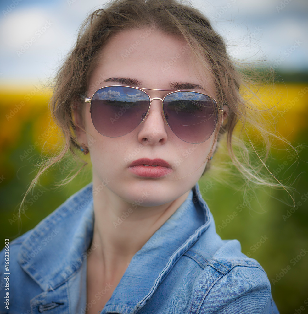 Attractive young blonde woman in a blue denim jacket, jeans, standing in a sunflowers field under a blue sky at Ukraine. Looking at camera. Attractive young blonde woman in a blue denim jacket, jeans, standing in a sunflowers field under a blue sky at Ukraine. Looking at camera.