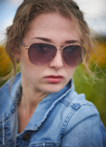 Attractive young blonde woman in a blue denim jacket, jeans, standing in a sunflowers field under a blue sky at Ukraine. Looking at camera. © Nikamata