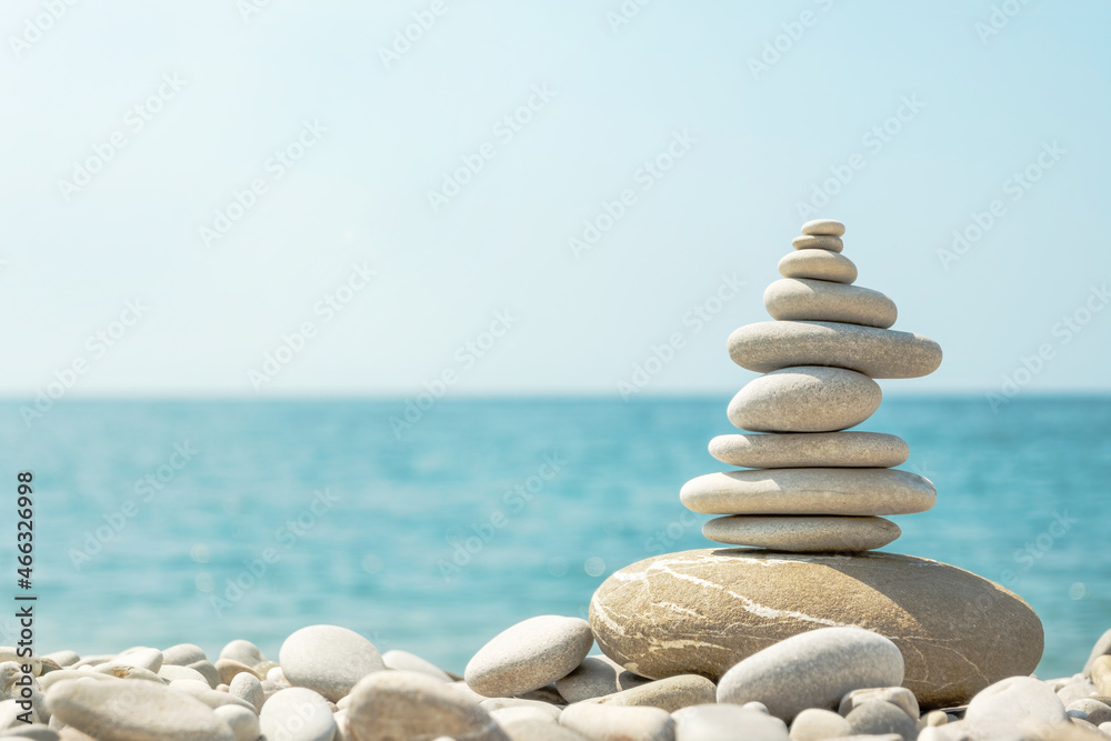 Fototapeta premium Balanced stack of pebbles on sea beach on sunny day. Natural summer harmony concept with stone pyramid on the coast.