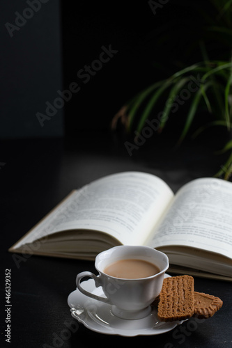 Reading a book with a  cup of coffee and two little biscuits