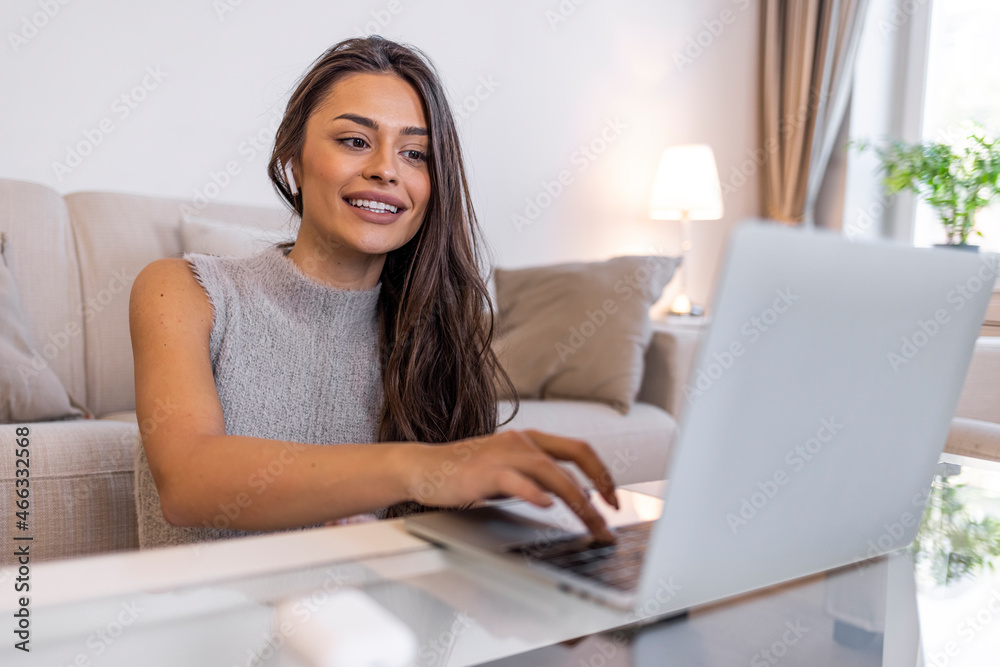 A young woman is using a laptop comfortably in the living room at home. Close up of a young woman using a laptop for teleconferencing at home. Young woman doing a video call on her laptop A young woman is using a laptop comfortably in the living room at home. Close up of a young woman using a laptop for teleconferencing at home. Young woman doing a video call on her laptop