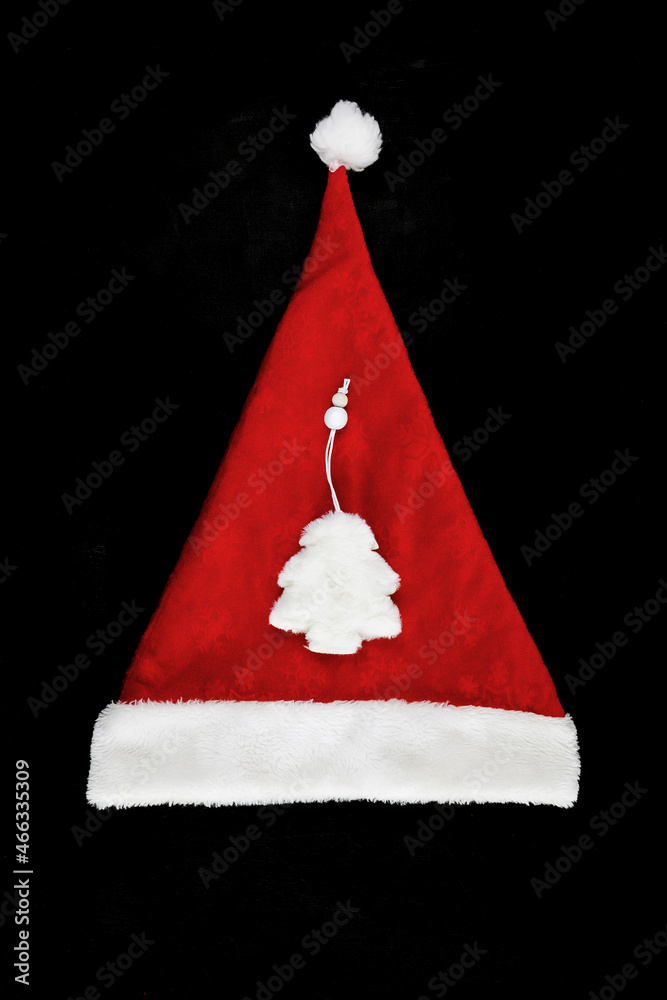 Christmas hat of santa claus with a white fluffy tree in the center on a black background. View from above Christmas hat of santa claus with a white fluffy tree in the center on a black background. View from above